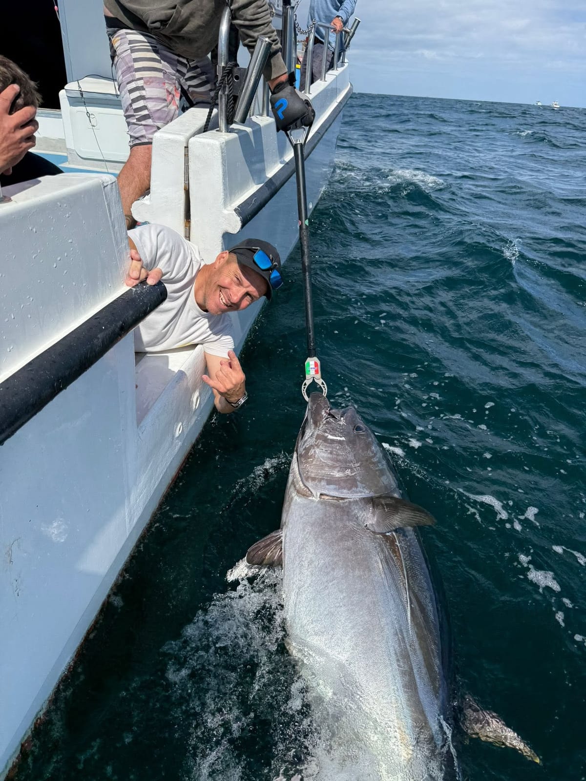 A giant bluefin tuna held alongside the boat on a lip grip while a grinning angler leans over the rail