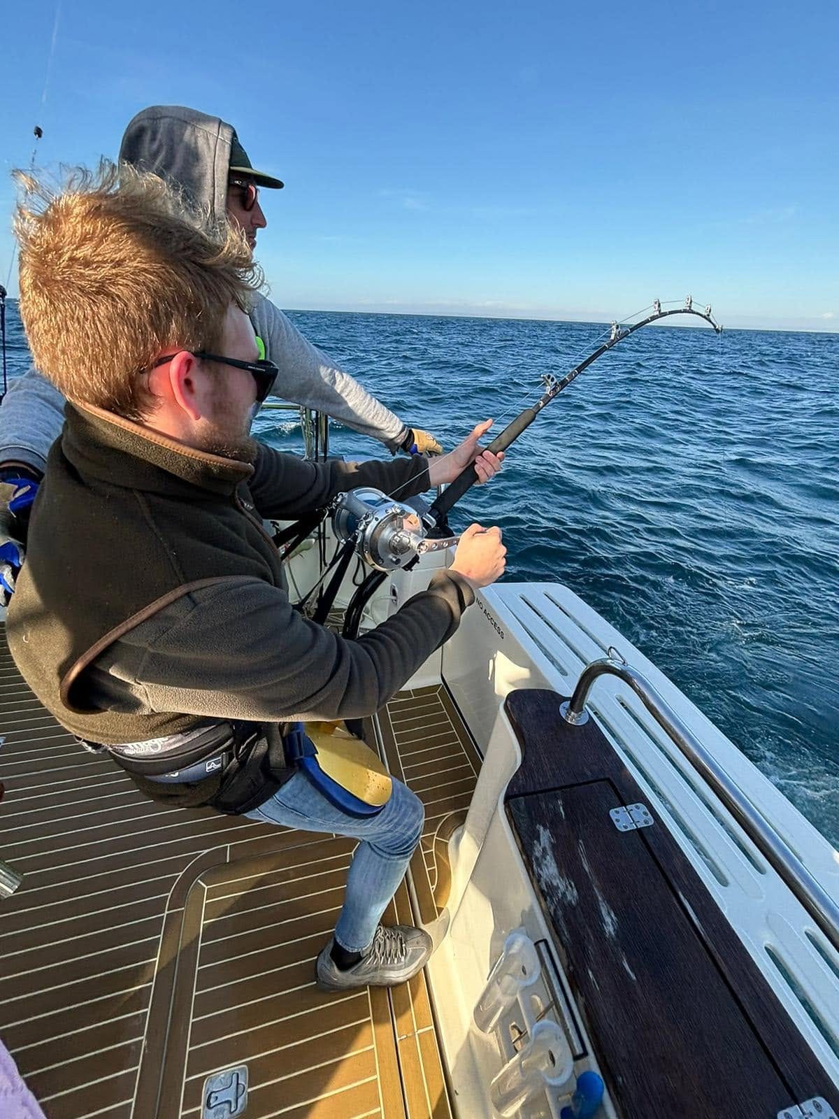A young angler in a harness bent into a tuna rod with the deckhand coaching behind him